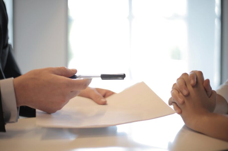 person holding pen and paper and person with hands crossed